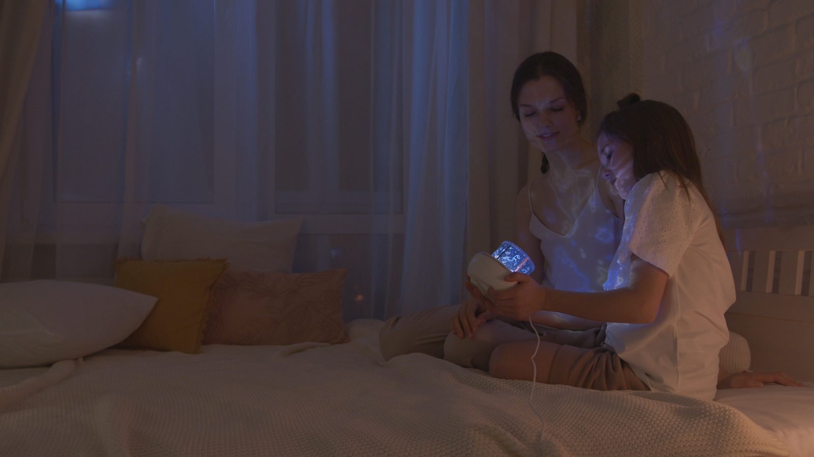 Mother and daughter relaxing together under a galaxy star projector in a cozy bedroom